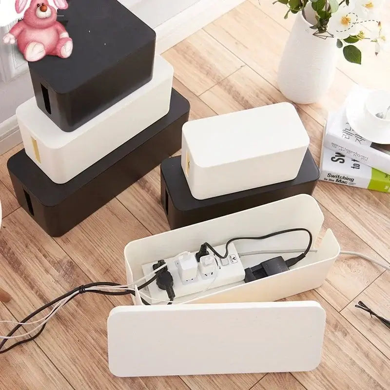 Boîtes de rangement pour câbles et multiprises en noir et blanc, organisant proprement les câbles électriques sur sol en bois.