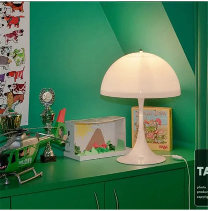 Lampadaire minimaliste LED champignon sur une table verte avec des jouets et des livres, créant une ambiance moderne et élégante.